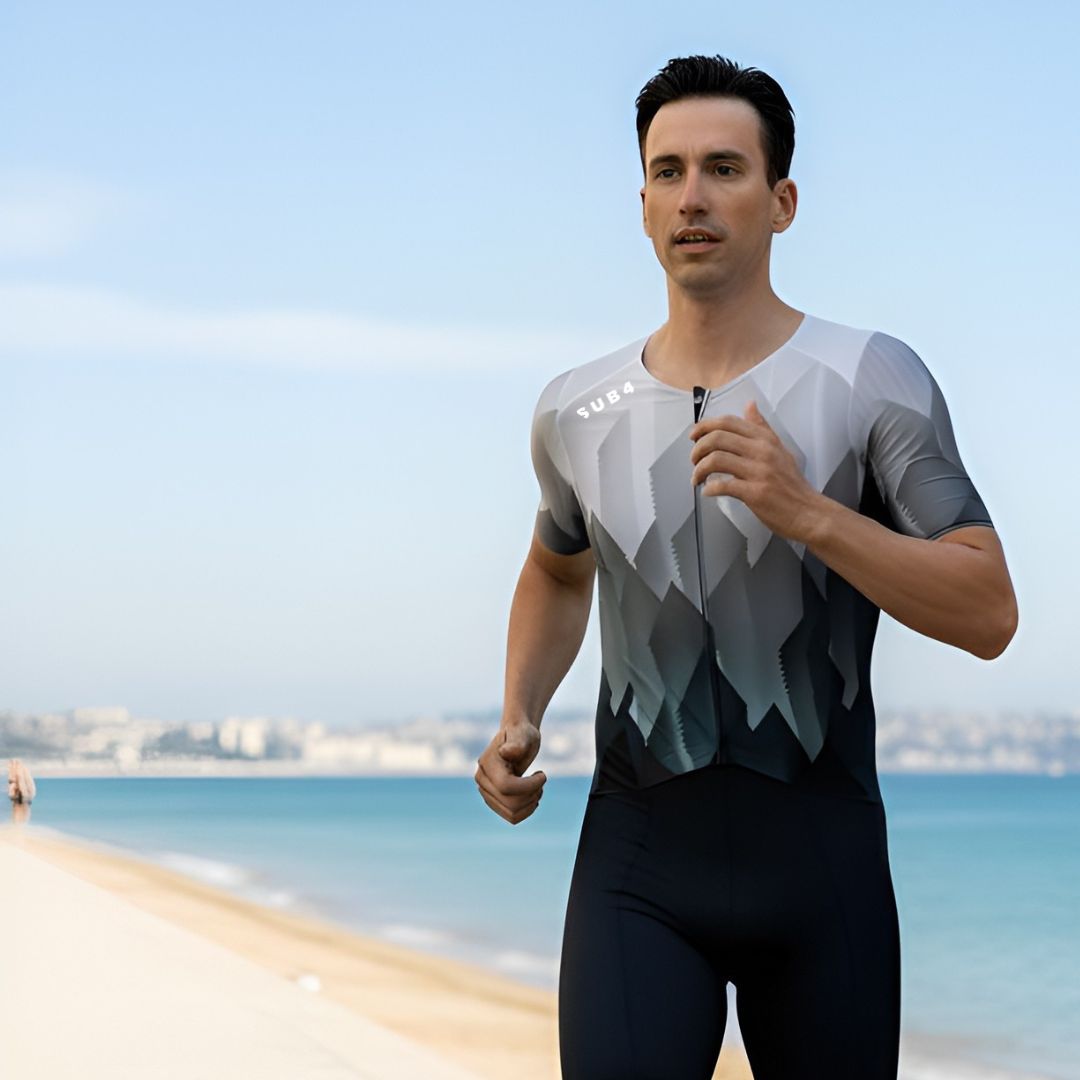 Man wearing a gray and black athletic outfit on a beach with ocean and sky in the background