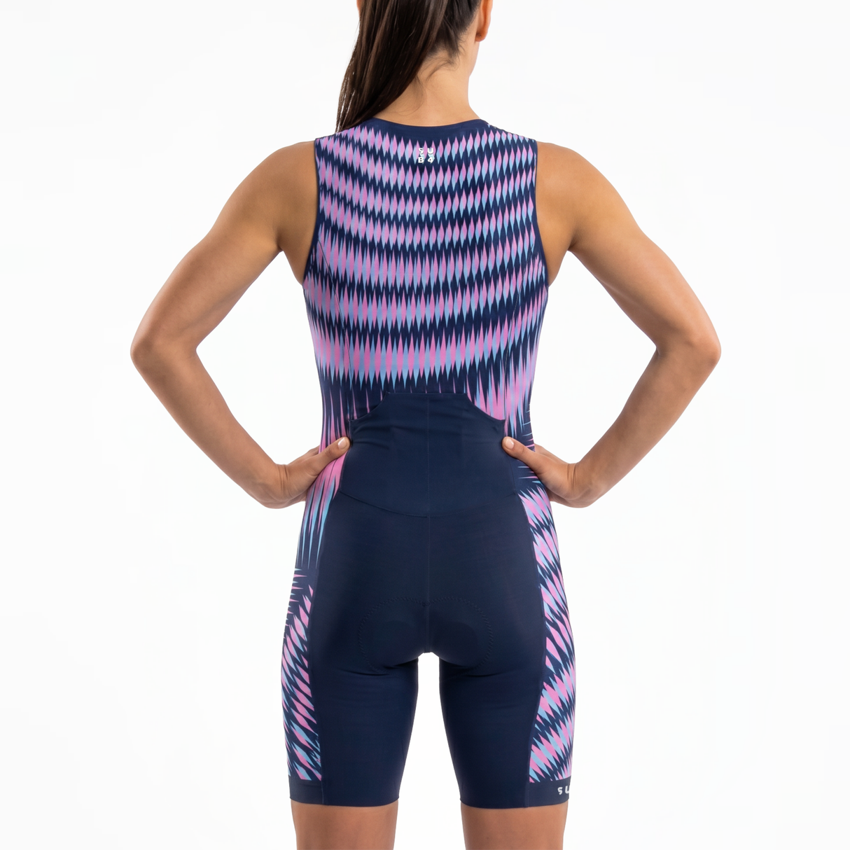 Rear view of a woman wearing a sleeveless Triathlon one-piece suit with a  blue base and pink and purple wavy geometric pattern, against a plain white background.