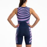 Rear view of a woman wearing a sleeveless Triathlon one-piece suit with a  blue base and pink and purple wavy geometric pattern, against a plain white background.